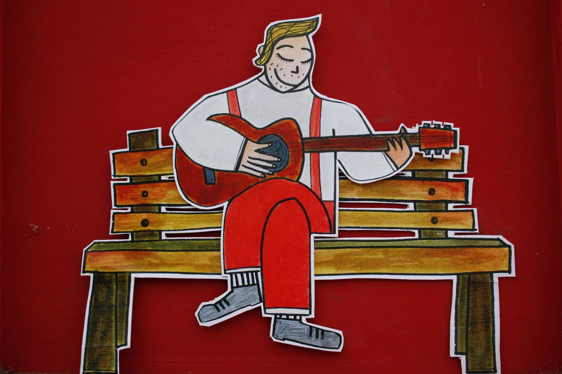 Un bonhomme de papier joue de la guitare sur un banc